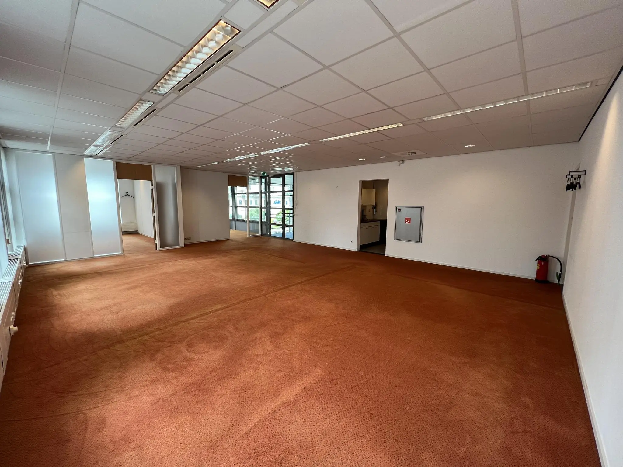 Lege kantoorruimte aan de Rivium 2e Straat met rood tapijt, systeemplafond en glazen wanden.